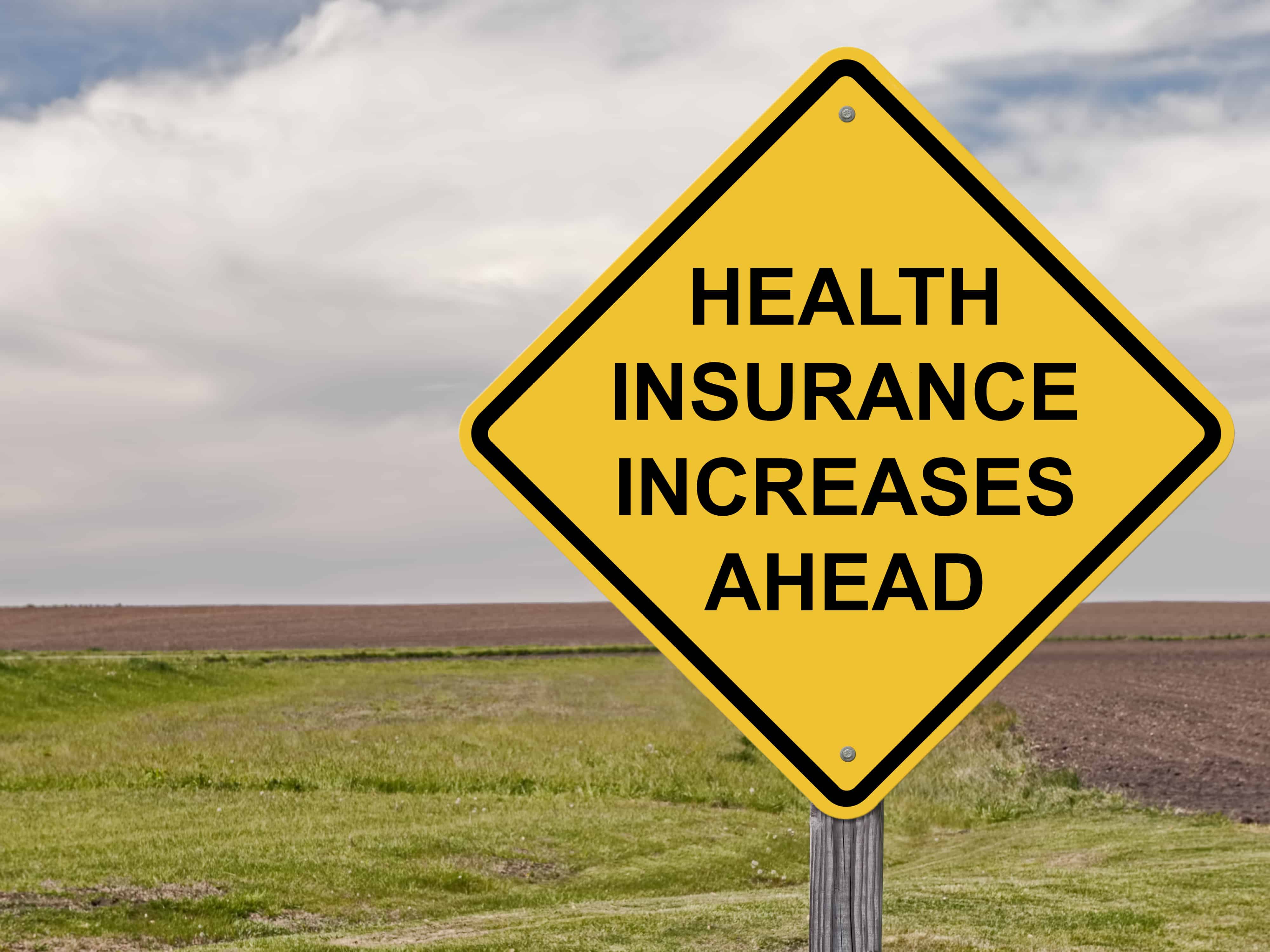 yellow road sign showing health insurance increases ahead