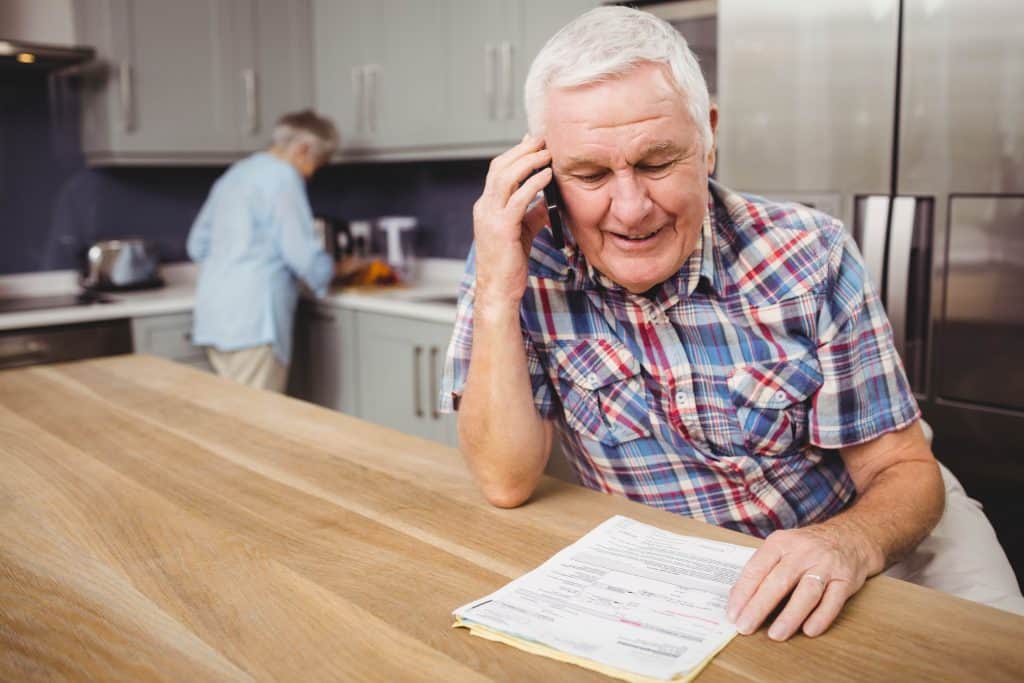 senior man holding bills on the phone and smiling