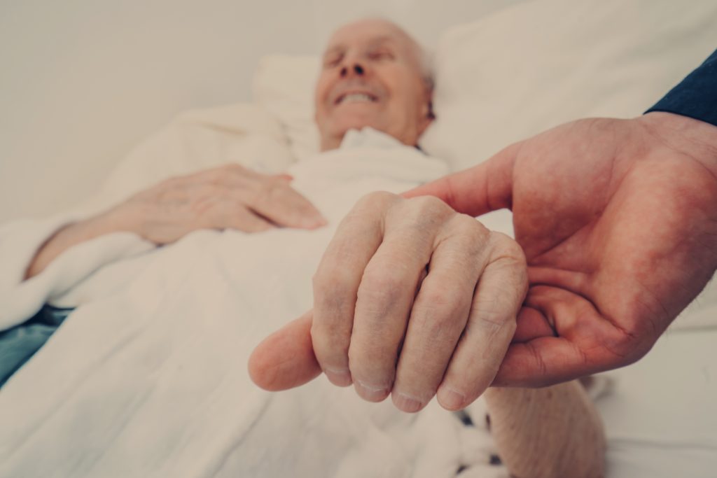 holding the hand of an elderly man in bed smiling